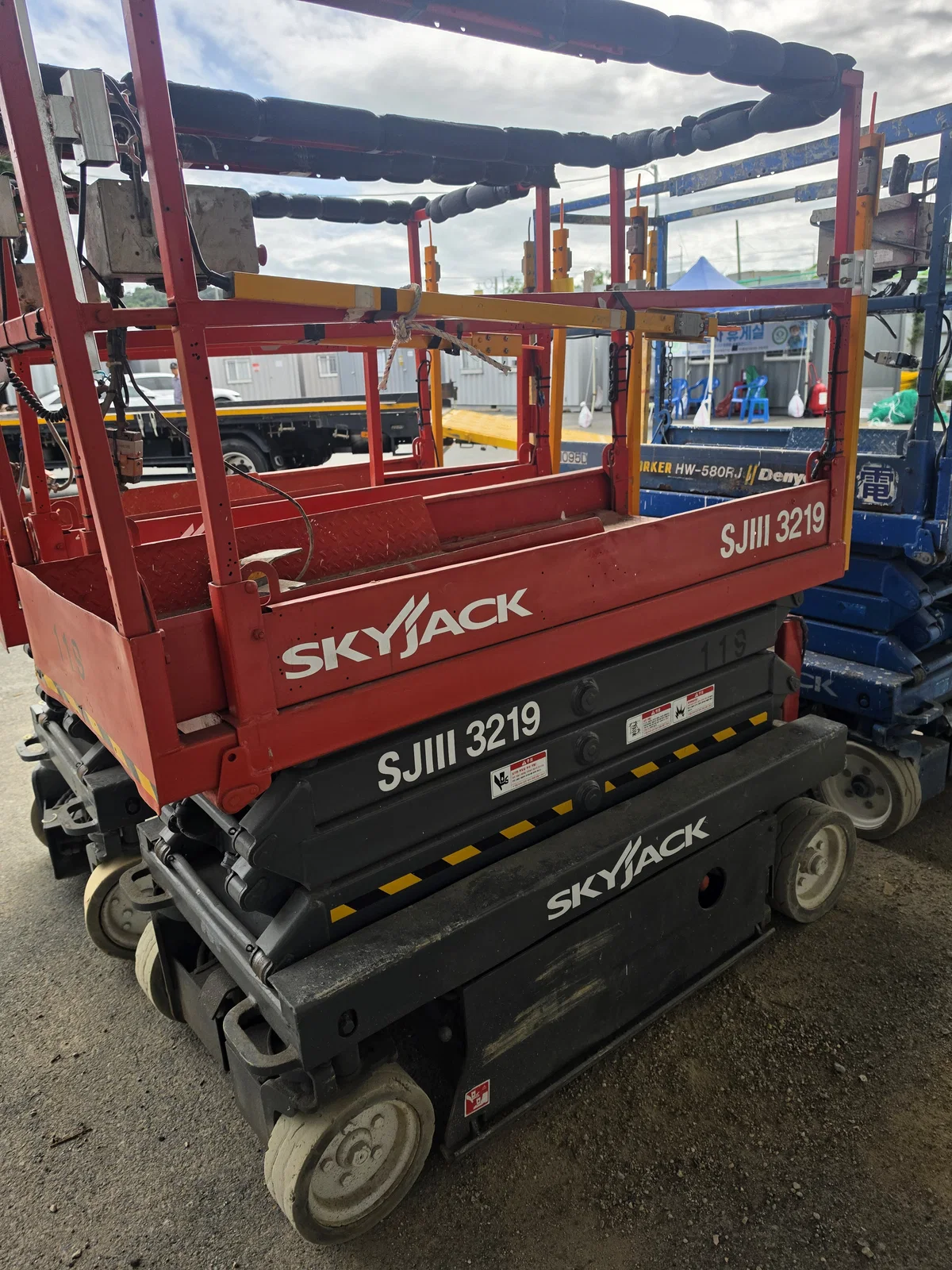 SKYJACK 시저리프트 근접, 나란히 주차된 다른 장비들